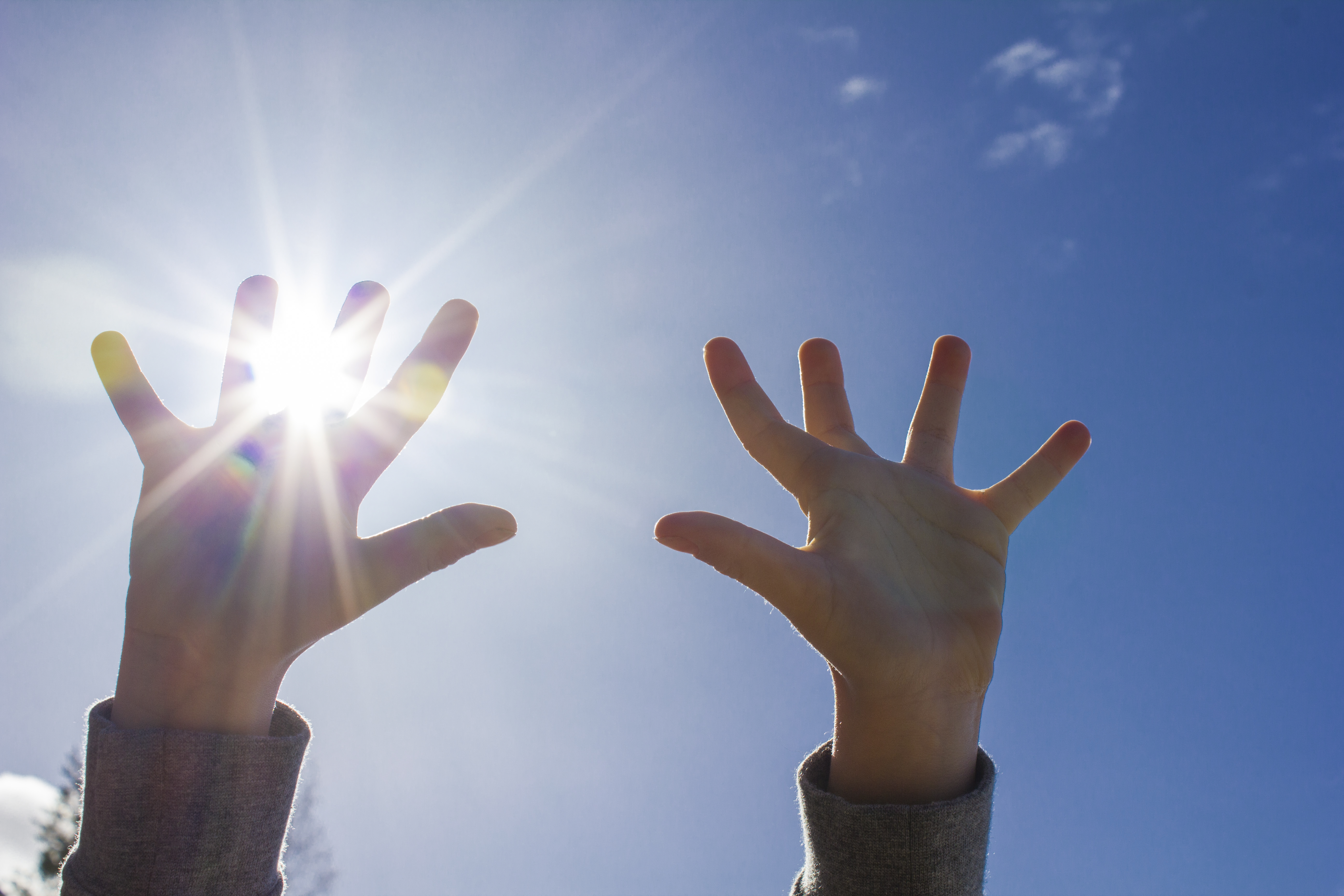 Ett barn sträcker upp händerna mot himlen. Solen lyser igenom fingrarna.